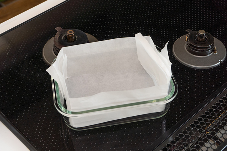 耐熱ガラス容器にクッキングシートを敷き、オーブンを160℃に予熱する。